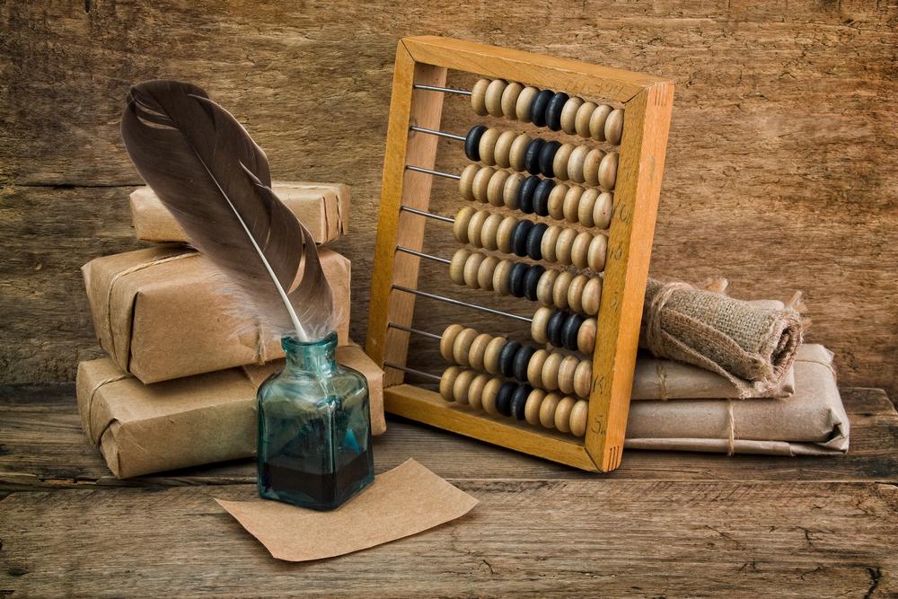 A wooden abacus, quill and bound books on a vintage writing desk